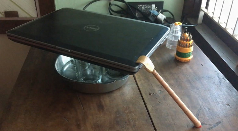dùng một thước gỗ hoặc chiếc muỗng có một đầu chạm vào laptop và đầu còn lại chạm vào thành khay